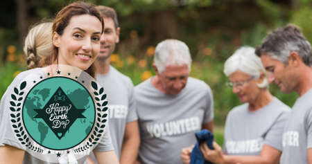 Composition of green globe logo and earth day text over volunteers cleaning up countryside. global...
