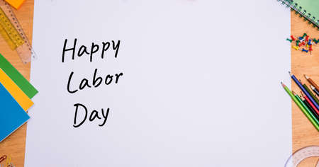Happy labor day text over white paper against multiple school equipment on wooden table. labor day celebration conceptの写真素材