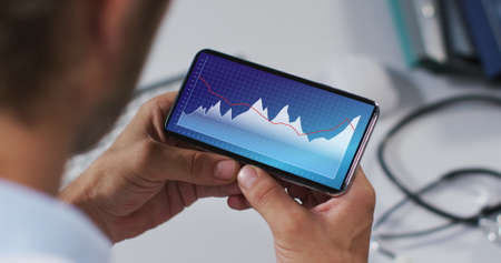 Hands of caucasian man using smartphone with statistics on screen. communication, data technology...