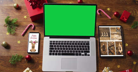 Laptop with green screen on screen, with smartphone,tablet and christmas decorations. christmas, festivity and communication technology digital composite image.の写真素材