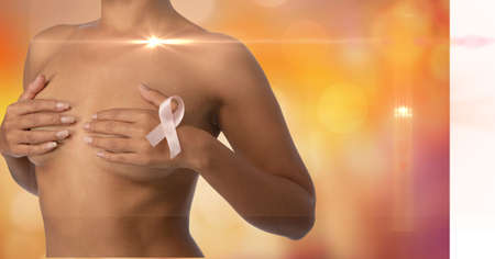Mid section of woman wearing a pink ribbon on her chest against spots of lights on orange background. breast cancer awareness and technology conceptの写真素材