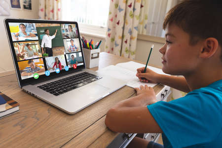 Caucasian boy using laptop for video call, with smiling diverse elementary school pupils on screen....