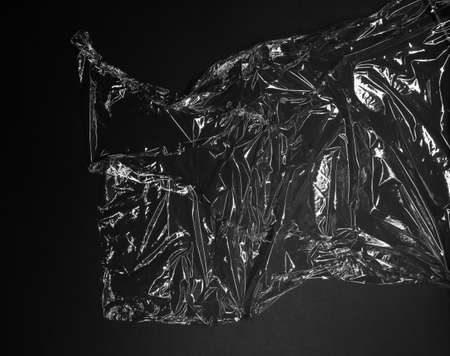 Reflecting light and shadow on creases and folds in scrunched clear plastic foil on black...