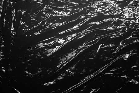 Reflecting light and shadow on creases and folds in black plastic sheeting. monochrome light and texture, abstract background image.の写真素材