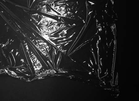Reflecting light and shadow on creases and folds in clear plastic foil on black background. monochrome light and texture, abstract background image.の写真素材