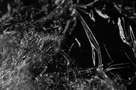 Reflecting light and shadow on creases and folds in scrunched clear plastic foil on black background. monochrome light and texture, abstract background image.の写真素材