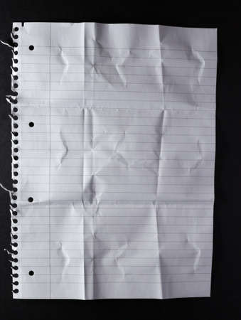 Folds and creases in hole punched sheet of lined paper with torn holes from spiral binding, on black. monochrome light and texture, abstract background image.の写真素材