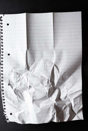 Hole punched sheet of lined paper, torn from spiral binding, folded and scrunched, on black. monochrome light and texture, abstract background image.の写真素材