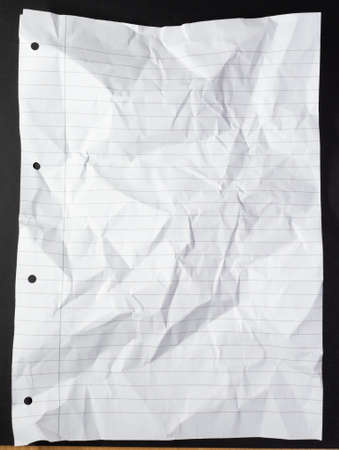 Light and shadow on creases in hole punched sheet of lined writing paper on black background. monochrome light and texture, abstract background image.の写真素材