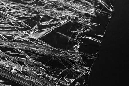 Reflecting light and shadow on creases and folds in clear plastic foil on black background. monochrome light and texture, abstract background image.の写真素材