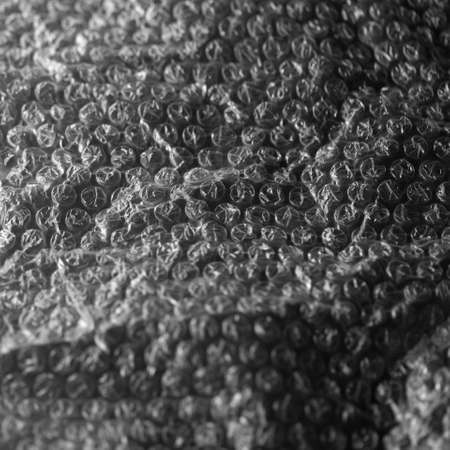 Reflecting light and shadow on creases and tears in plastic wrap sheeting on black. monochrome light and texture, abstract background image.の写真素材