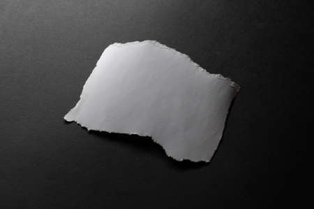 Roughly torn rectangle of white paper on black background. monochrome light and texture, abstract background image.の写真素材