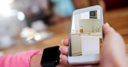 Image of person using smartphone with house kitchen interiors displayed on screen. Online shopping house decorating concept digital composite.の写真素材