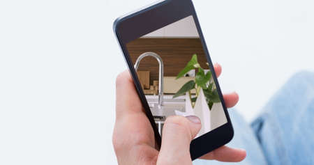 Image of person using smartphone with house kitchen interiors displayed on screen. Online shopping house decorating concept digital composite.の写真素材