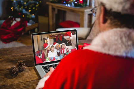 Caucasian santa claus on christmas laptop video call with caucasian family. christmas, festivity and communication technology.の写真素材