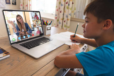 Caucasian boy using laptop for video call, with waving diverse high school pupils on screen....