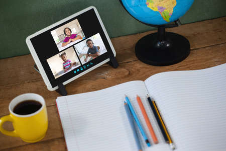Smiling diverse elementary school pupils during class on tablet screen. communication technology and online education, digital composite image.の写真素材