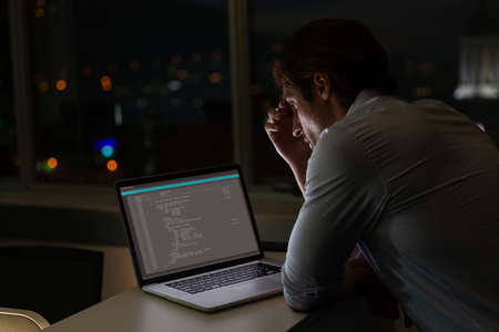 Caucasian male programmer sitting at desk, using laptop with coding on screen. coding, programming and computer technology digital composite image.の写真素材
