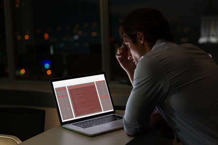 Caucasian male programmer sitting at desk, using laptop with coding on screen. coding, programming...