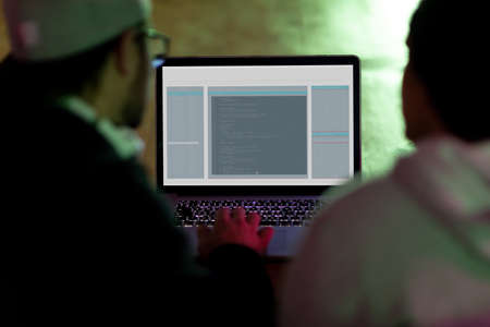 Back view of two diverse male colleagues at desk using computer with coding on screen. coding, programming and computer technology digital composite image.の写真素材