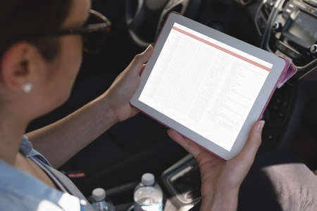 Biracial female programmer sitting in car and using tablet with coding on screen. coding,...