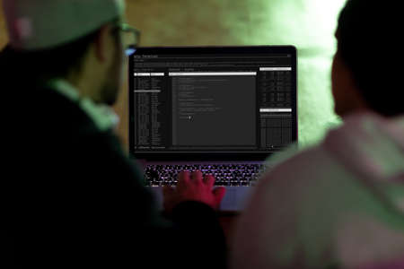 Back view of two diverse male colleagues using laptop with coding on screen. coding, programming and computer technology digital composite image.の写真素材