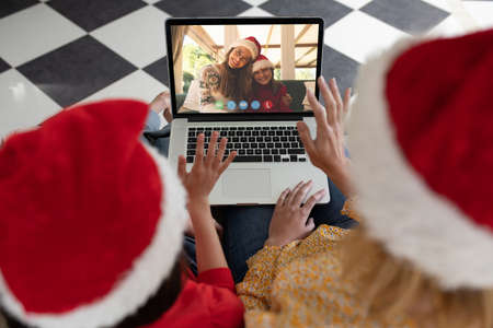 Caucasian mother and daughter in santa hats on christmas laptop video call with friends. christmas, festivity and communication technology.の写真素材