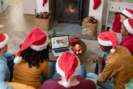 Biracial family in santa hats on christmas laptop video call with friend. christmas, festivity and communication technology.の写真素材