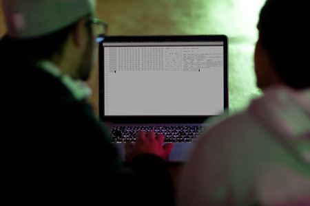 Back view of two diverse male colleagues using laptop with coding on screen. coding, programming and computer technology digital composite image.の写真素材