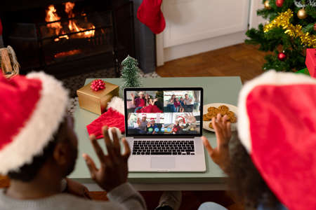 African american couple in santa hats on christmas laptop video call with friends. christmas, festivity and communication technology.の写真素材