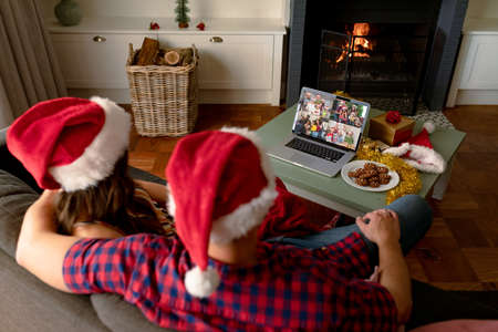 Caucasian couple in santa hats on christmas laptop video call with friends. christmas, festivity and communication technology.の写真素材
