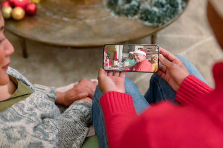 Biracial women on christmas smartphone video call with smiling family. christmas, festivity and...