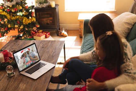 Caucasian mother and daughter in santa hats on christmas laptop video call with smiling friends. christmas, festivity and communication technology.の写真素材