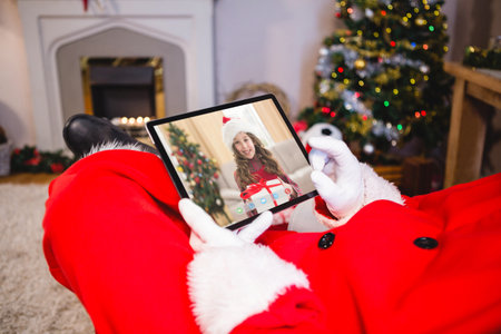Santa claus making christmas laptop video call with happy caucasian girl in santa hat. christmas, festivity and communication technology.の写真素材