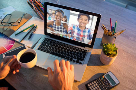 Hands of man using laptop for video call, with smiling diverse high school pupils on screen. communication technology and online education, digital composite image.の写真素材