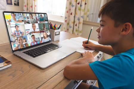 Caucasian boy using laptop for video call, with smiling diverse elementary school pupils on screen....