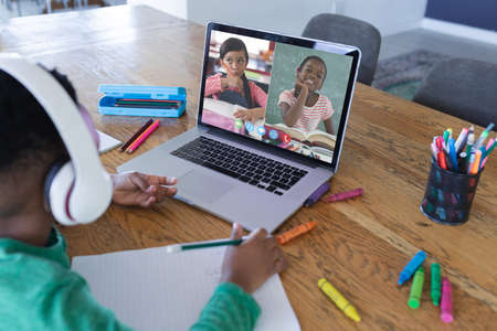 African american boy using laptop for video call, with diverse elementary school pupils on screen. communication technology and online education, digital composite image.の写真素材