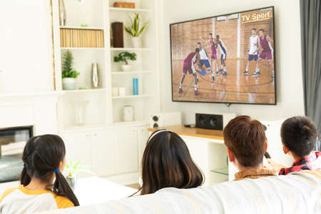 Rear view of family sitting at home together watching basketball match on tv. sports, competition,...