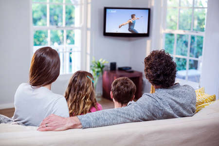 Family watching television while sitting on sofa at homeの写真素材