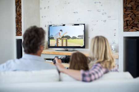 Rear view of family sitting at home together watching cricket match on tv. sports, competition, entertainment and technology concept digital composite image.の写真素材