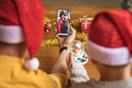 Caucasian father and son in santa hats making smartphone christmas video call with diverse friends. christmas, festivity and communication technology.の写真素材