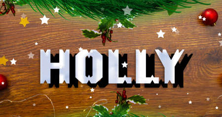 Image of holly text over stars falling and christmas decoration on table. christmas, winter, tradition and celebration concept digitally generated image.の写真素材
