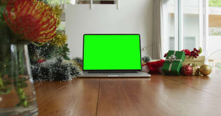 Laptop with green screen copy space on table with santa hats, christmas tree and presents. christmas, festivity and communication technology.の写真素材