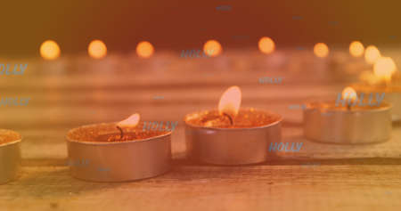 Image of holly text in blue over lit tea light candles. christmas, tradition and celebration concept digitally generated image.の写真素材