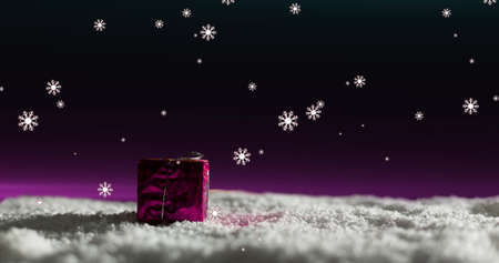 Image of snow falling over christmas present with pink light in a night sky. christmas, tradition and celebration concept digitally generated image.の写真素材