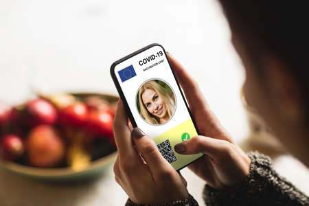 Woman holding smartphone with covid 19 vaccine passport. global covid 19 pandemic concept digitally generated video.の写真素材