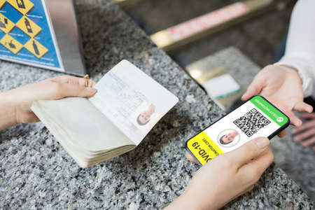 Woman holding documents and smartphone with covid 19 vaccine passport. global covid 19 pandemic concept digitally generated video.の写真素材