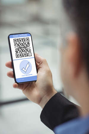 Man holding smartphone with covid 19 vaccine passport. global covid 19 pandemic concept digitally generated video.の写真素材