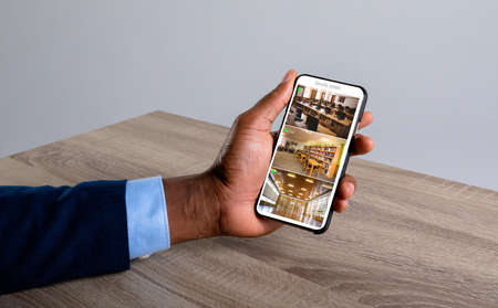 Hand of caucasian man holding smartphone with view from security cameras at library on screen. security, safety, surveillance, and digital interface.の写真素材