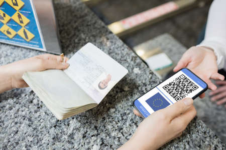 Woman at airport holding documents smartphone with covid 19 vaccine passport. global covid 19 pandemic concept digitally generated video.の写真素材